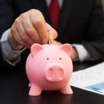 Close-up of a businessman putting money in a piggy bank